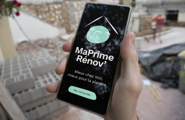 Main qui tient un téléphone avec l'application MaPrimeRénov' ouverte