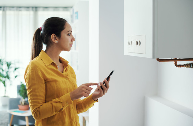 Femme qui regarde le compteur de son chauffe-eau avec un téléphone à la main