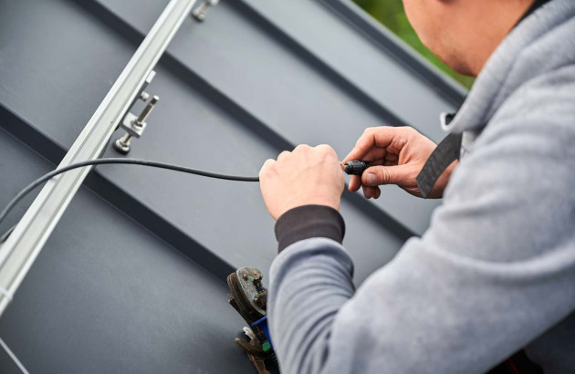 Installateur de panneau solaire qui effectue un branchement de câbles sur une installation