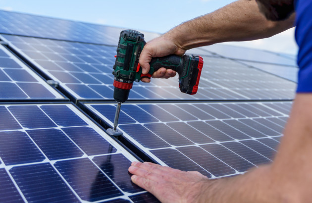 Homme qui utilise une visseuse pour fixer des panneaux solaires sur un bac lesté