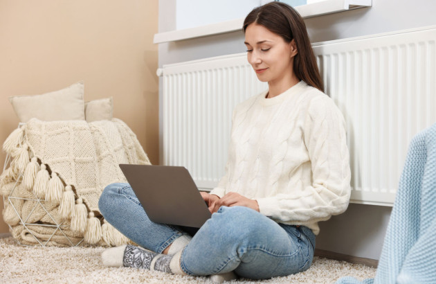 Femme assise contre son radiateur qui utilise un ordinateur portable