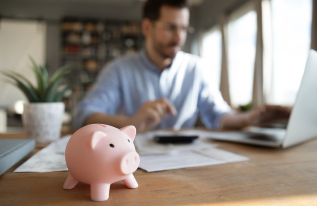 Homme sur un pc avec une tirelire cochon en premier plan