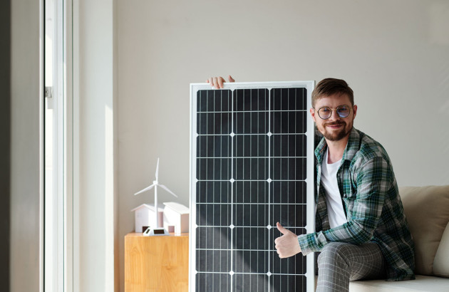 Homme assis qui tient un panneau solaire, pouce vers le haut