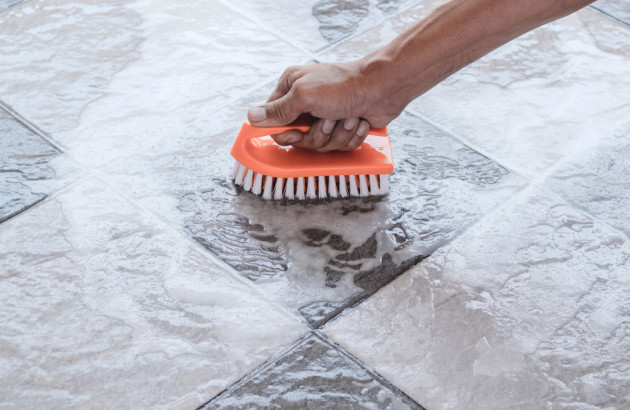 Personne qui nettoie son carrelage en frottant avec une brosse et de la mousse