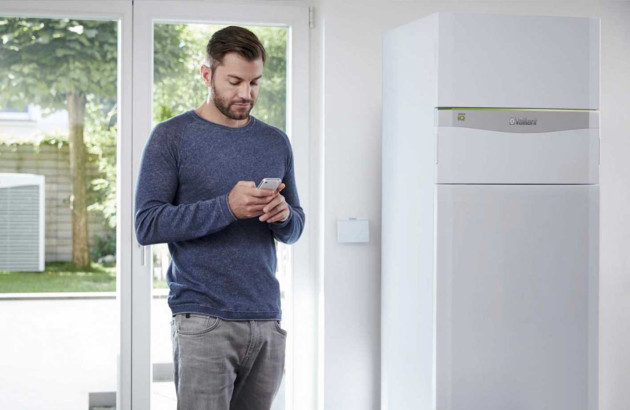 Homme qui consulte son téléphone à côté d'une unité intérieur de pompe à chaleur géothermique