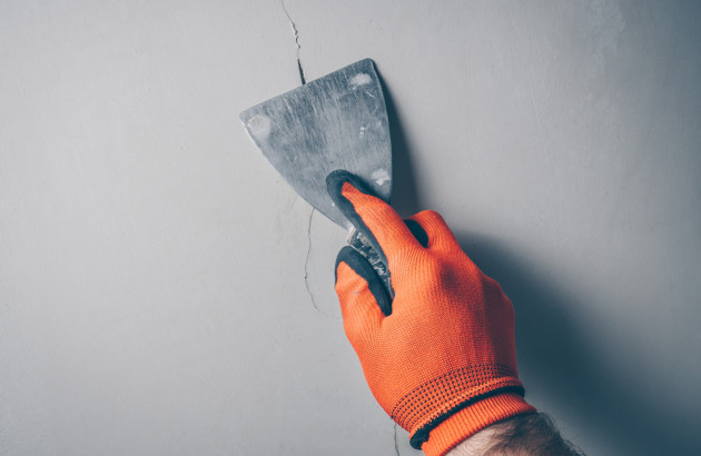 Un artisan répare une fissure dans un mur à l'aide d'une spatule.