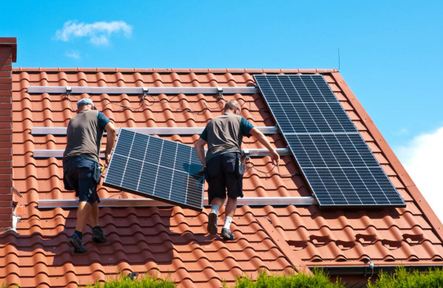 Hommes plaçant deux panneaux solaires sur le toit d'une maison