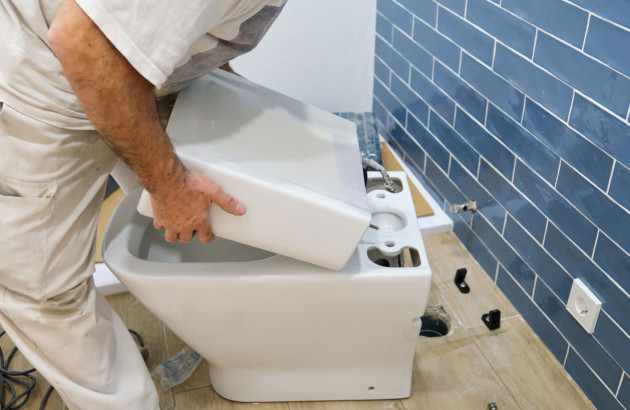 Artisan en train d'installer une chasse d'eau sur des toilettes