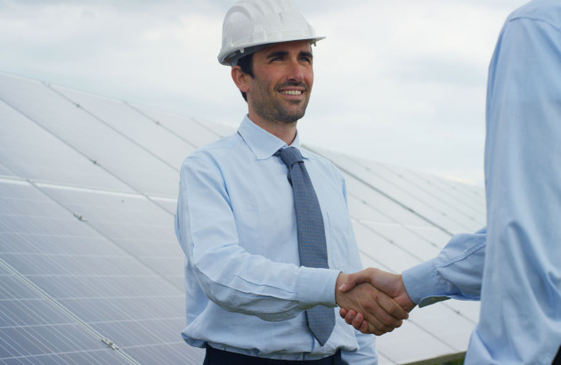 Chef de chantier qui sert la main à une autre personne devant une installation de panneaux solaires