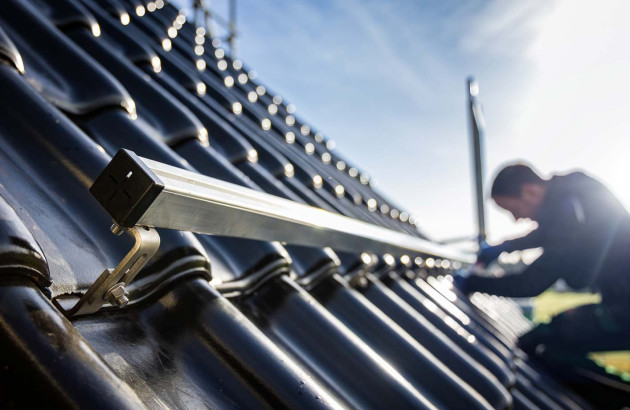 Ouvrier qui installe un rail de fixation de panneau solaire sur un toit de maison