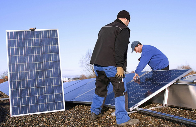 3 ouvriers qui posent des panneaux solaires sur des supports fixés sur un toit plat