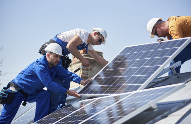 3 professionnels qui posent un panneau solaire sur un toit de maison