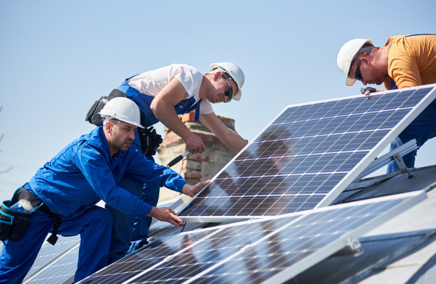 3 installateurs qui posent un panneau solaire sur un toit